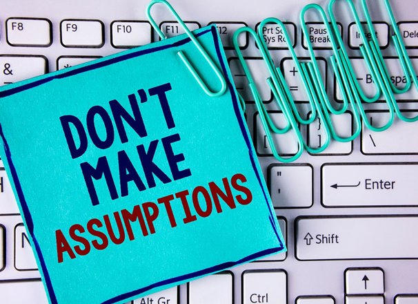Note saying "don't make assumptions" and paper clips on a keyboard