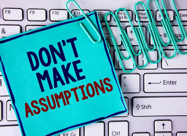 Note saying "don't make assumptions" and paper clips on a keyboard