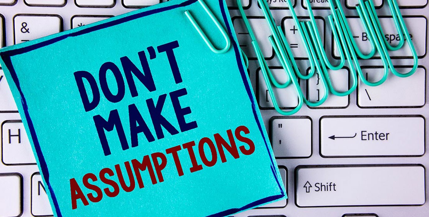 Note saying "don't make assumptions" and paper clips on a keyboard