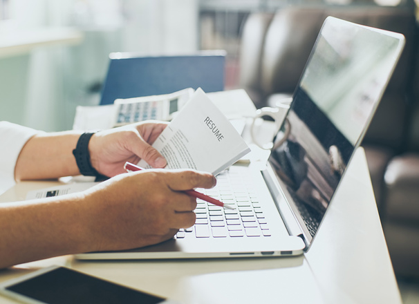 Hands holding a resume and pencil on top of an open laptop