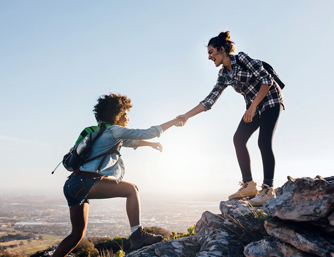 Friends helping each other climb up a hill