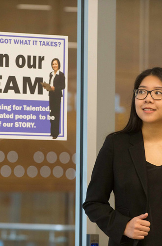 Person wearing business attire standing in the doorway with a "Join our team" sign posted