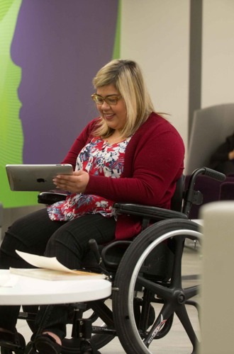Student holding a tablet while chatting with a friend in a campus common room