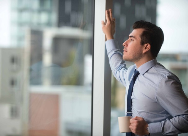 Person wearing business attire holding a mug and looking out a large window