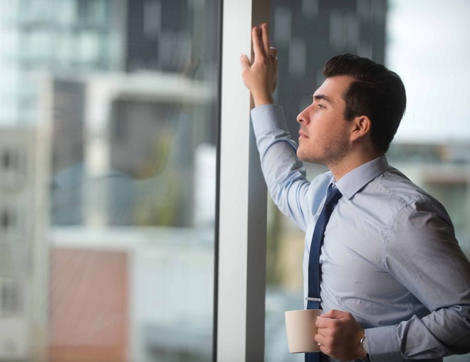 Person wearing business attire holding a mug and looking out a large window