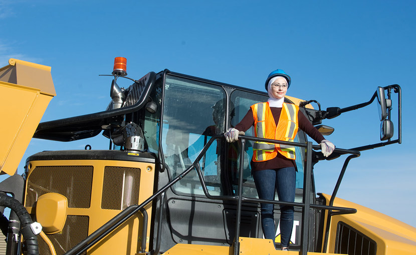 Person wearing hard hat and safety vest standing on top of heavy machinery