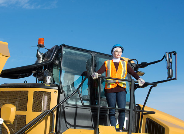 Person wearing hard hat and safety vest standing on top of heavy machinery