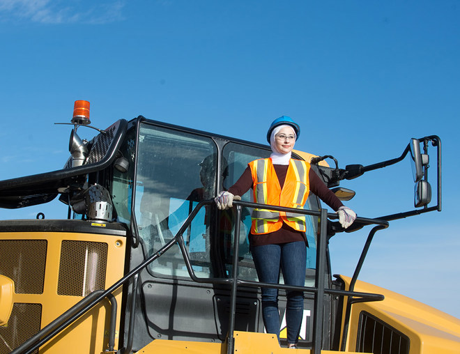 Person wearing hard hat and safety vest standing on top of heavy machinery