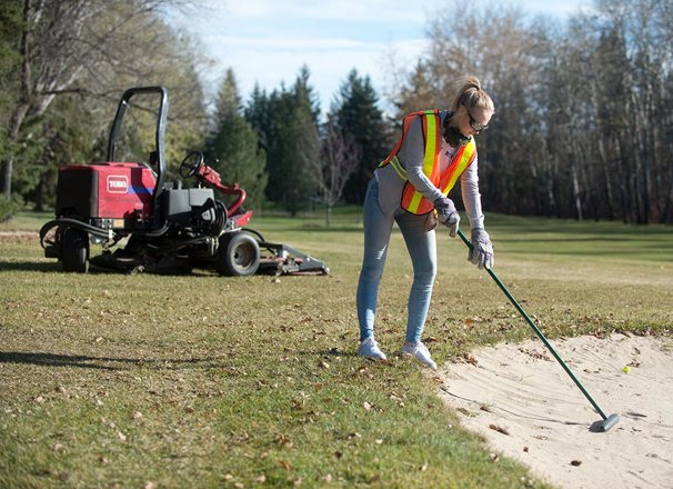 Golf course groundskeeper working on a sand bunker