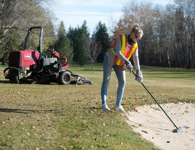 Golf course groundskeeper working on a sand bunker