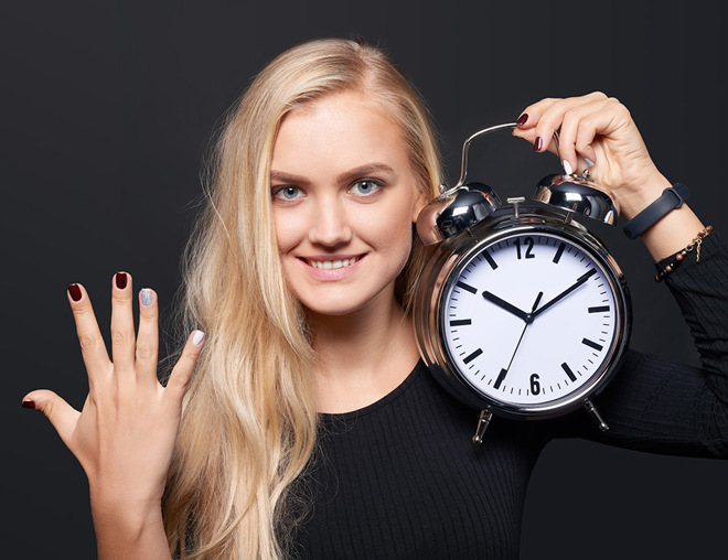 Person holding up 5 fingers and holding an alarm clock
