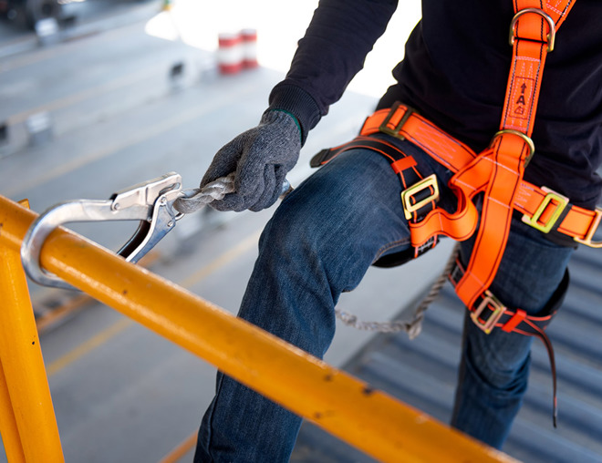 Construction worker wearing an orange harness with safety hook on railing