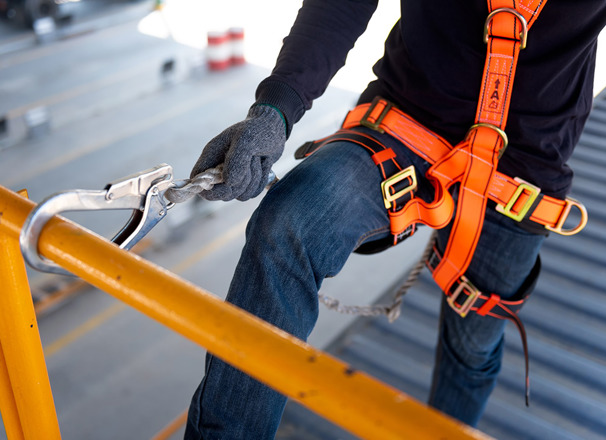 Construction worker wearing an orange harness with safety hook on railing