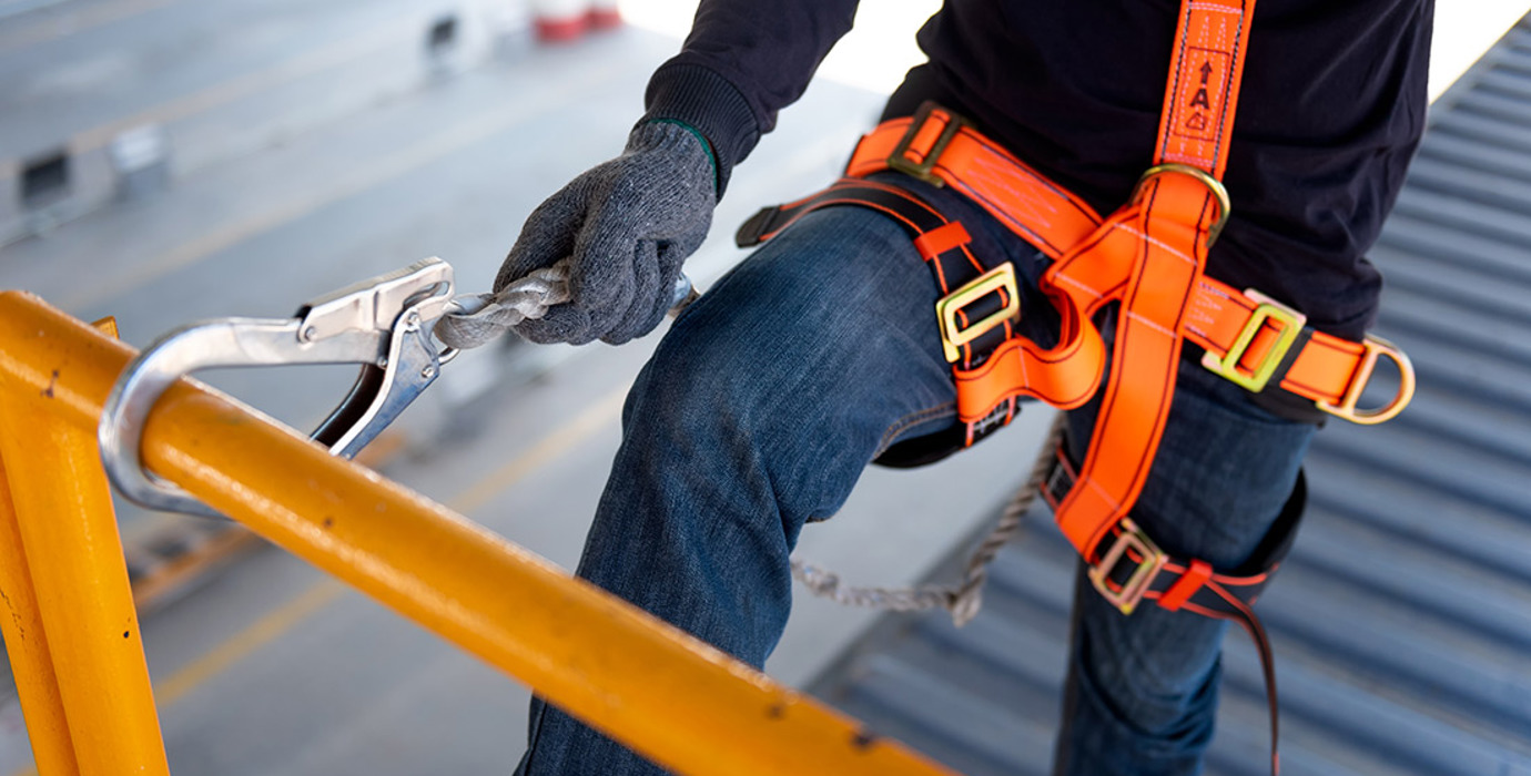 Construction worker wearing an orange harness with safety hook on railing