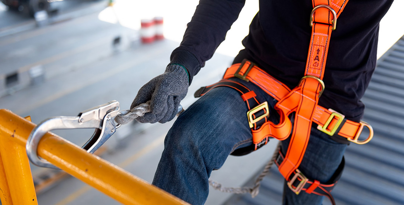 Construction worker wearing an orange harness with safety hook on railing