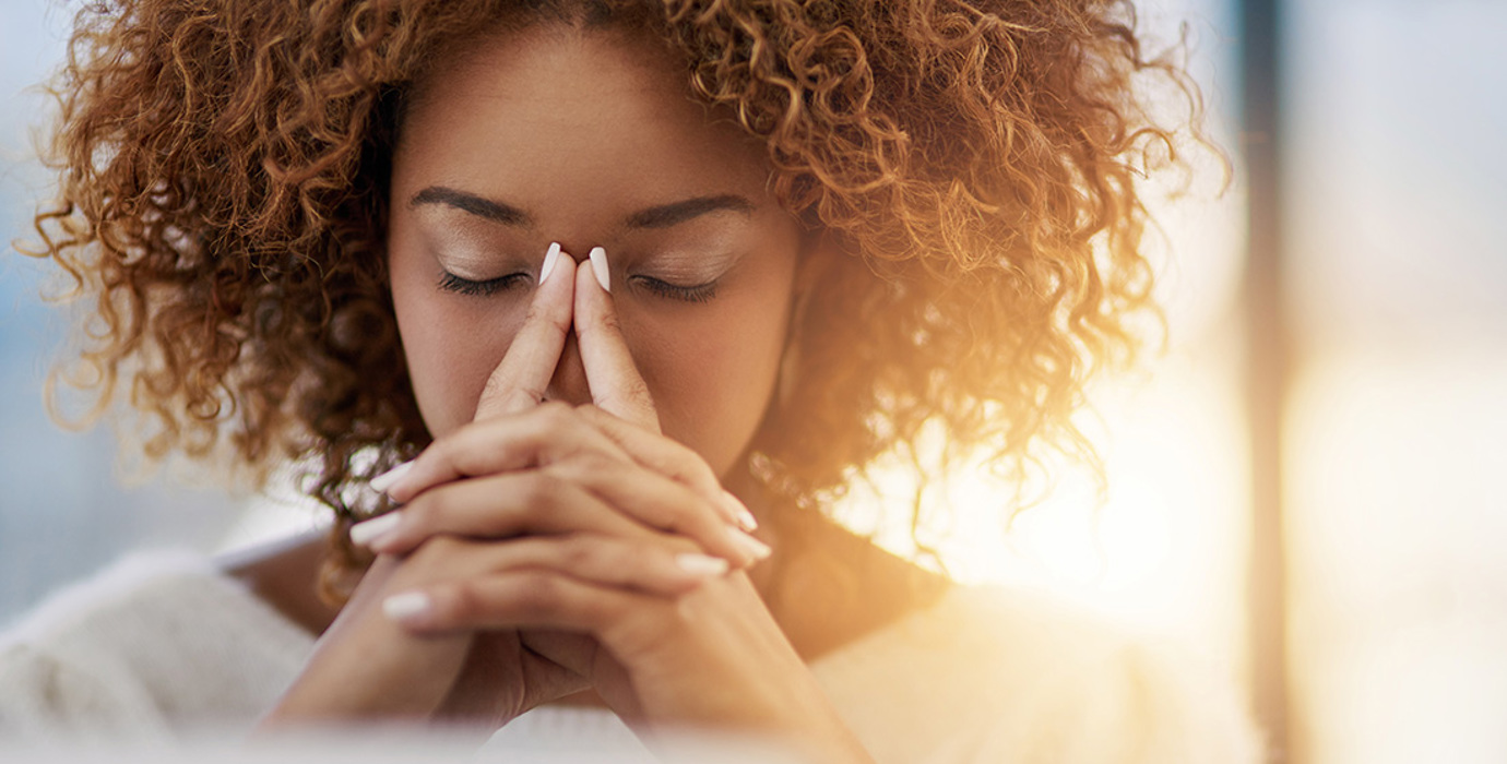 Person with eyes closed, fingers tented in front of face