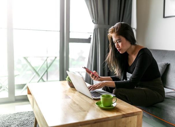 Person sitting on a couch in the living room looking at a laptop and smartphone