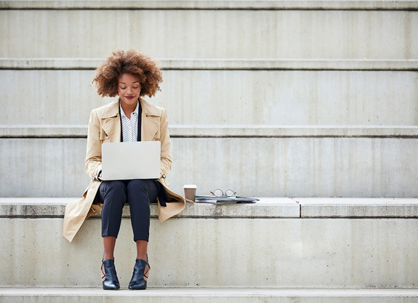 Person in office attire sitting on steps outside with laptop