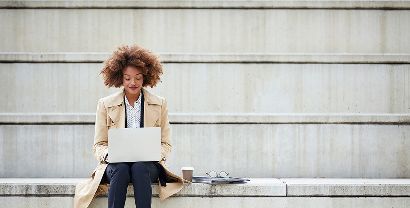 Person in office attire sitting on steps outside with laptop