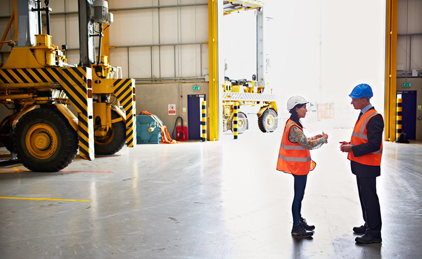 Employee and manager wearing hard hats discussing in a warehouse