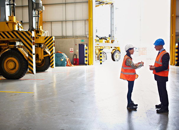 Employee and manager wearing hard hats discussing in a warehouse