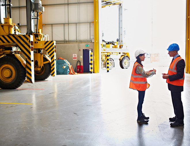 Employee and manager wearing hard hats discussing in a warehouse