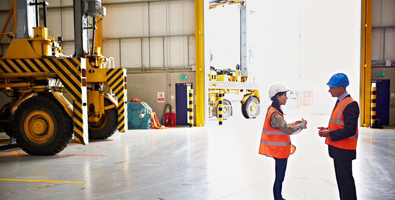 Employee and manager wearing hard hats discussing in a warehouse