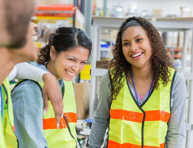Employees wearing safety vests smiling in a warehouse