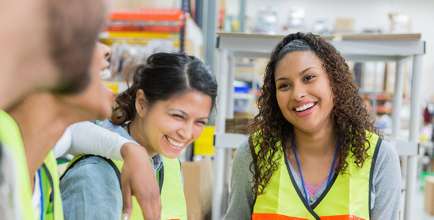 Employees wearing safety vests smiling in a warehouse
