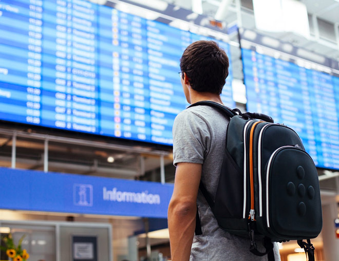 Travelling youth with backpack looking at arrival/departure board at an airport