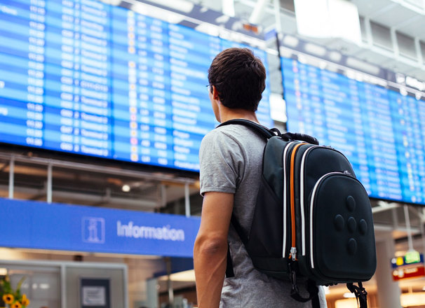 Travelling youth with backpack looking at arrival/departure board at an airport