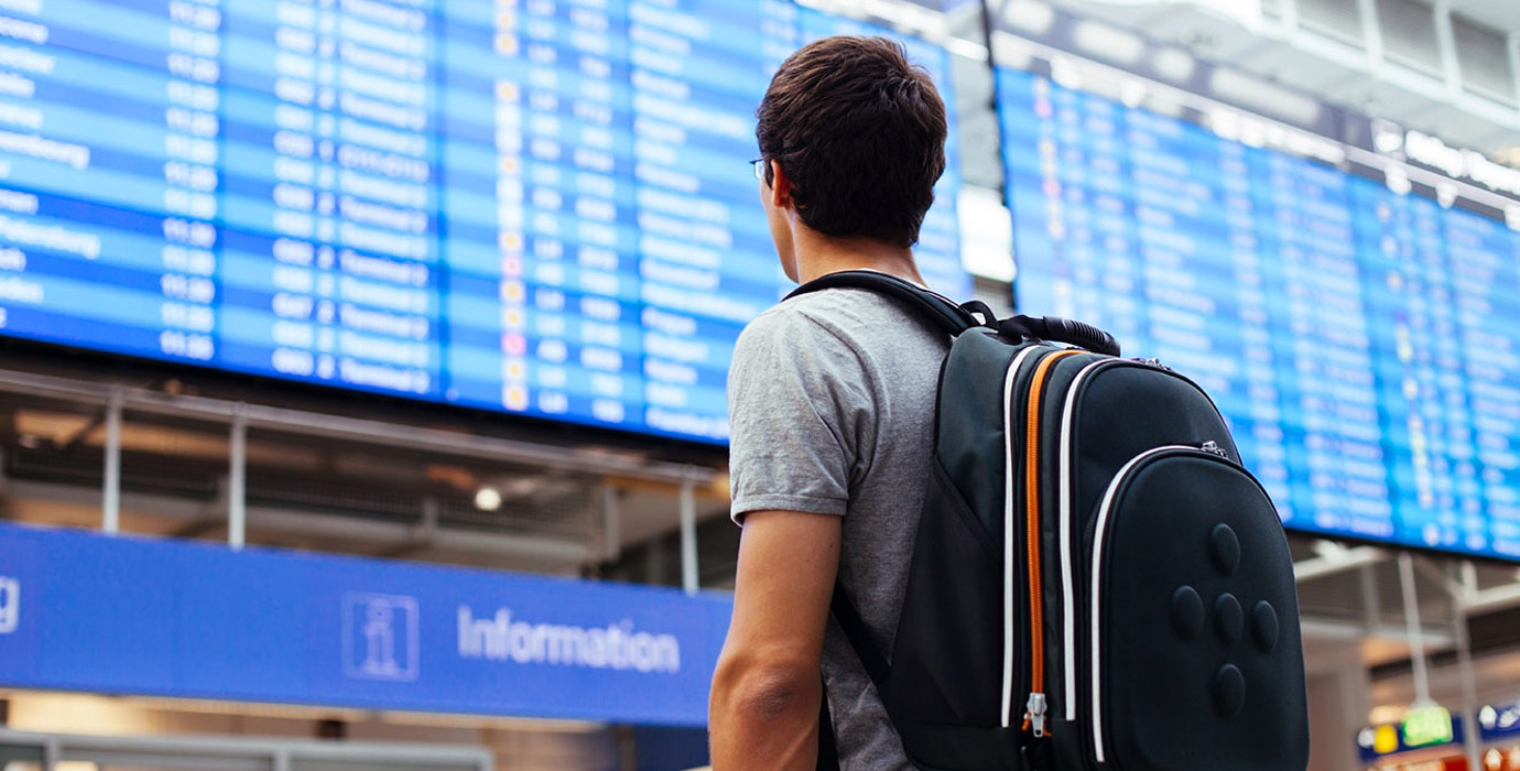 Travelling youth with backpack looking at arrival/departure board at an airport