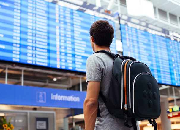 Travelling youth with backpack looking at arrival/departure board at an airport