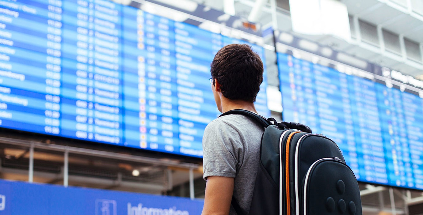 Travelling youth with backpack looking at arrival/departure board at an airport