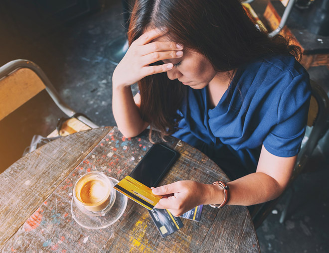 Person having a coffee with head in hand unhappily holding a credit card