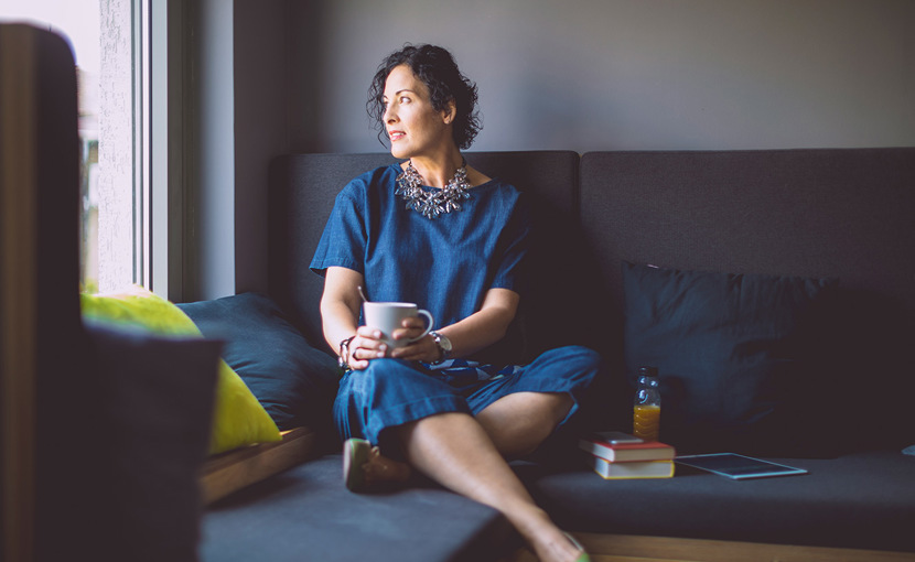 Person sitting on a couch looking out the window while holding a mug
