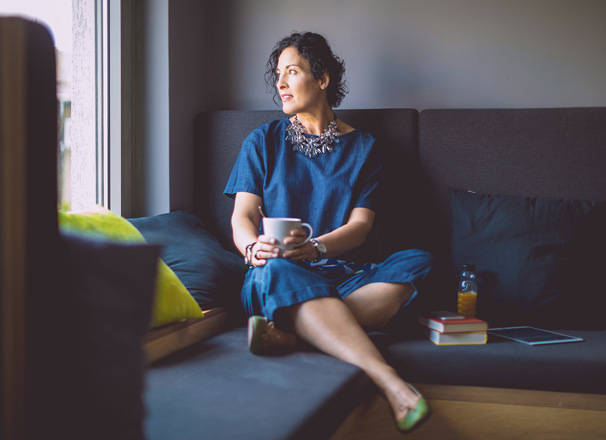 Person sitting on a couch looking out the window while holding a mug