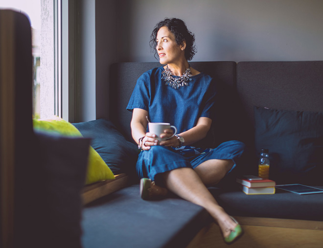 Person sitting on a couch looking out the window while holding a mug