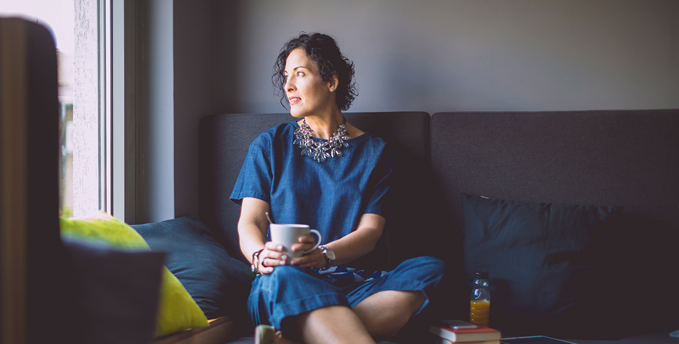 Person sitting on a couch looking out the window while holding a mug