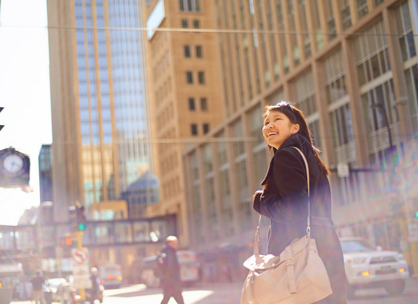Person carrying a messenger bag and smiling while walking in a downtown area