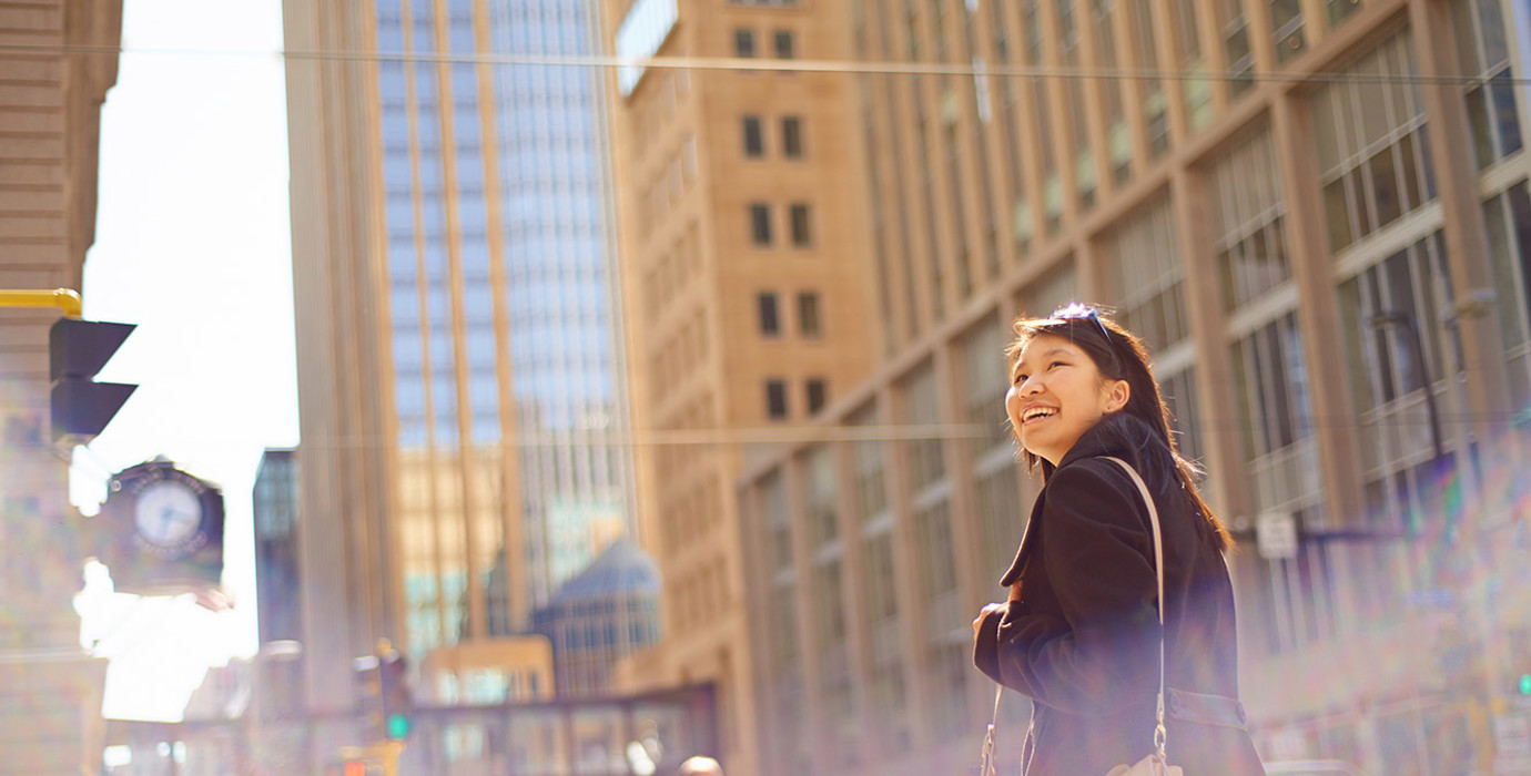 Person carrying a messenger bag and smiling while walking in a downtown area