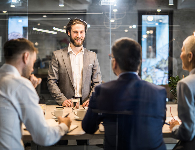 Person in a boardroom standing in front of 3 others during a meeting