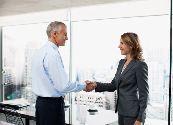 2 people in a boardroom shaking hands and smiling