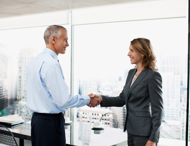 2 people in a boardroom shaking hands and smiling