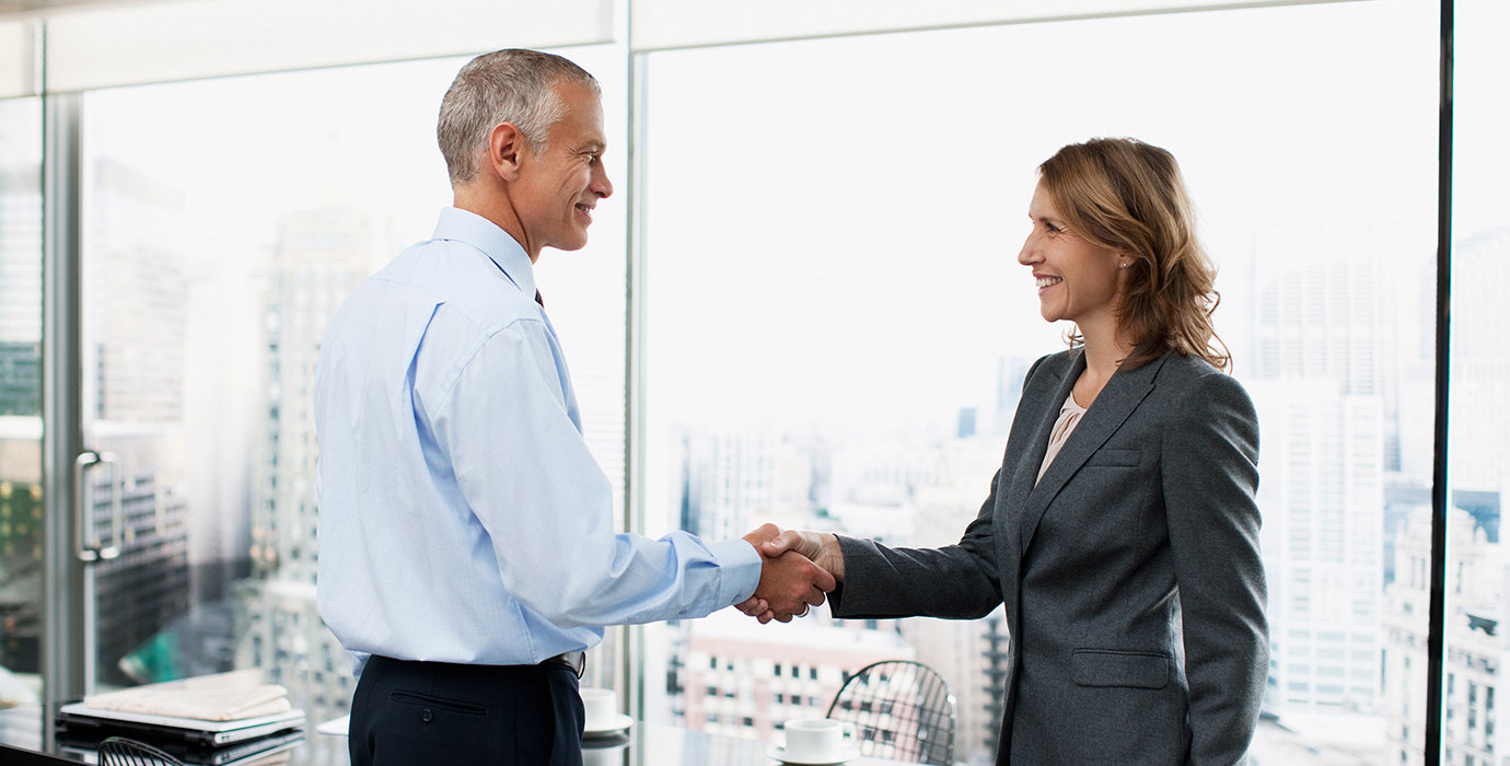 2 people in a boardroom shaking hands and smiling