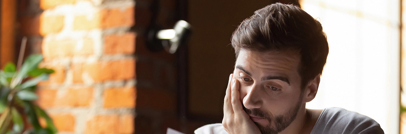 Worried person with chin in his hand reading a document in his other hand