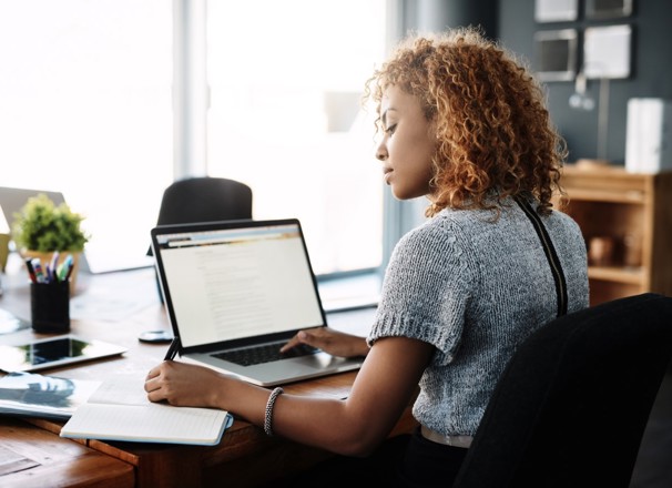 Person writing in a notebook with a laptop open on the desk