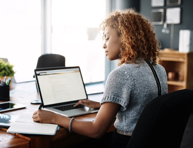 Person writing in a notebook with a laptop open on the desk