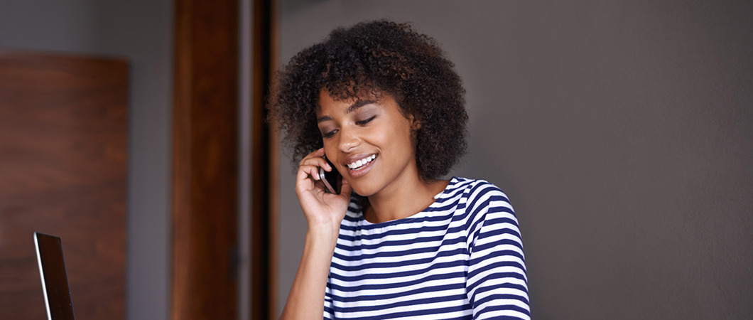 Person wearing a striped shirt, sitting at a table and talking on the phone while taking notes