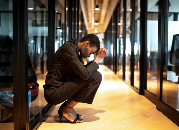 Worried person with head in hands crouched in an office hallway